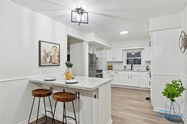 kitchen featuring sink, stainless steel refrigerator, a breakfast bar, white cabinets, and kitchen peninsula