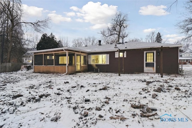 snow covered rear of property featuring a sunroom