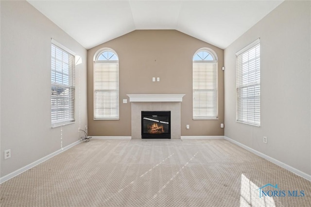 unfurnished living room with a tiled fireplace, lofted ceiling, and light colored carpet