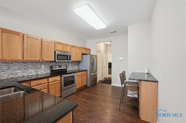 kitchen featuring dark stone countertops, backsplash, stainless steel appliances, a kitchen bar, and kitchen peninsula