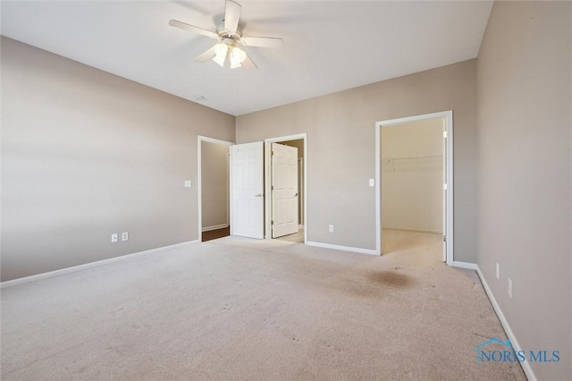 unfurnished bedroom featuring a spacious closet, light colored carpet, a closet, and ceiling fan