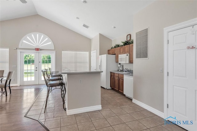 kitchen with vaulted ceiling, a kitchen island, a breakfast bar, light tile patterned floors, and white appliances