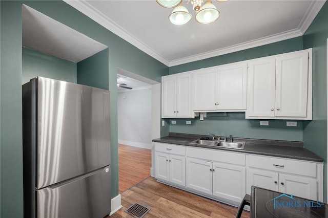 kitchen with sink, white cabinets, stainless steel fridge, ornamental molding, and light hardwood / wood-style flooring