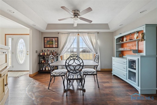 dining area featuring a raised ceiling, ceiling fan, and dark hardwood / wood-style flooring