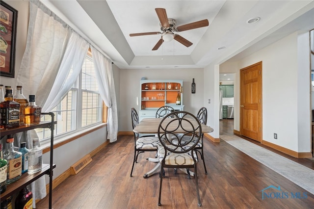 dining space with a raised ceiling, ceiling fan, and dark hardwood / wood-style flooring