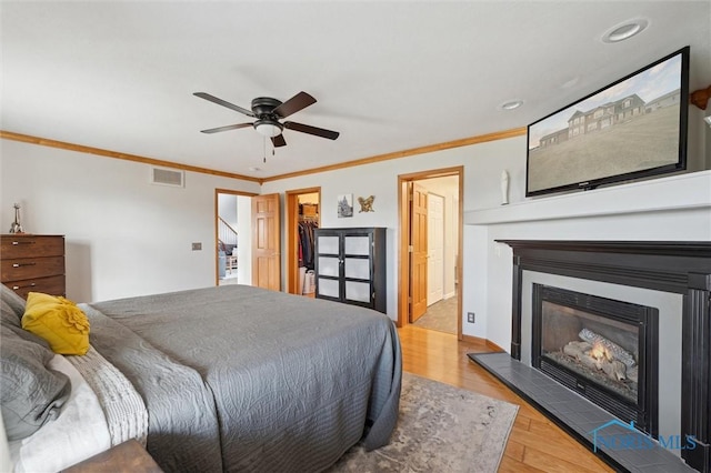 bedroom featuring crown molding, ceiling fan, a fireplace, a walk in closet, and a closet