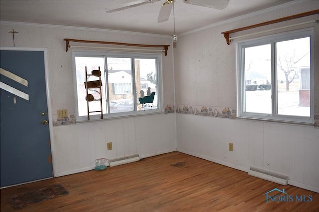 empty room featuring baseboard heating, ornamental molding, a healthy amount of sunlight, and hardwood / wood-style floors