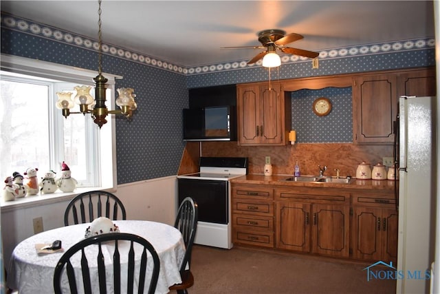 kitchen featuring ceiling fan with notable chandelier, pendant lighting, sink, dark colored carpet, and white appliances