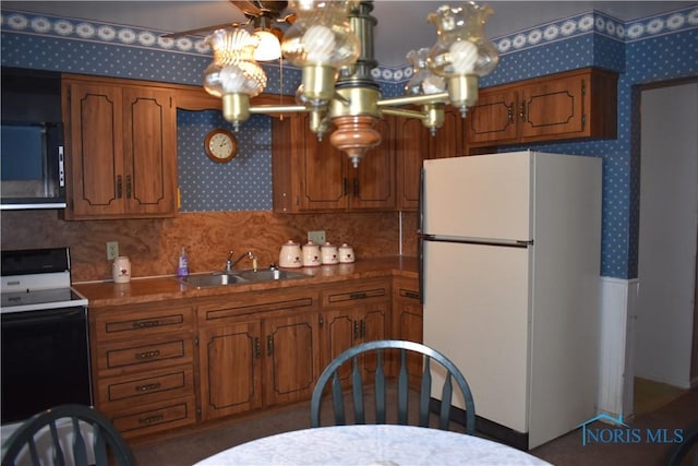 kitchen with sink, an inviting chandelier, backsplash, black range with electric cooktop, and white fridge