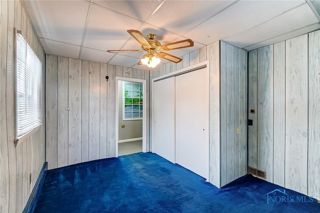 unfurnished bedroom featuring ceiling fan, wood walls, a closet, and dark colored carpet