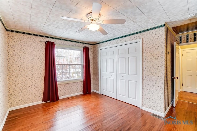 unfurnished bedroom featuring ceiling fan, wood-type flooring, a closet, and ornamental molding