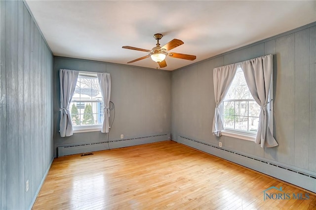 empty room featuring baseboard heating, ceiling fan, and light wood-type flooring