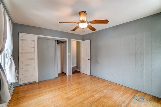 unfurnished bedroom with ceiling fan, wood walls, a closet, and light wood-type flooring