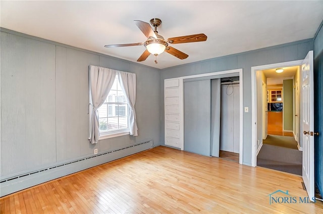 unfurnished bedroom featuring light hardwood / wood-style flooring, a closet, ceiling fan, and baseboard heating