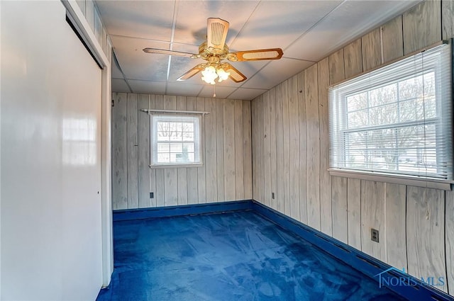 spare room featuring dark carpet, ceiling fan, and wood walls