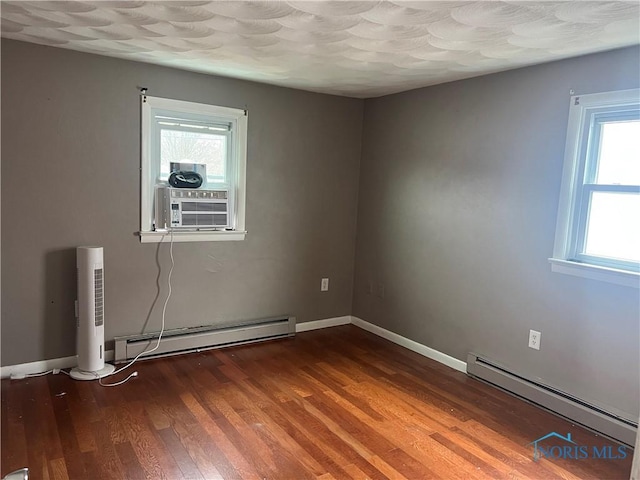 spare room with baseboard heating, hardwood / wood-style floors, and a wealth of natural light