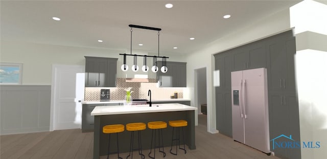 kitchen featuring gray cabinets, white refrigerator with ice dispenser, an island with sink, decorative backsplash, and decorative light fixtures