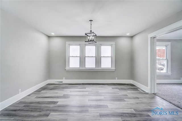 unfurnished dining area featuring an inviting chandelier and light hardwood / wood-style flooring