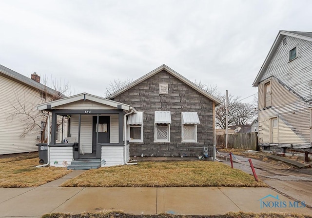 bungalow with covered porch, fence, and a front lawn