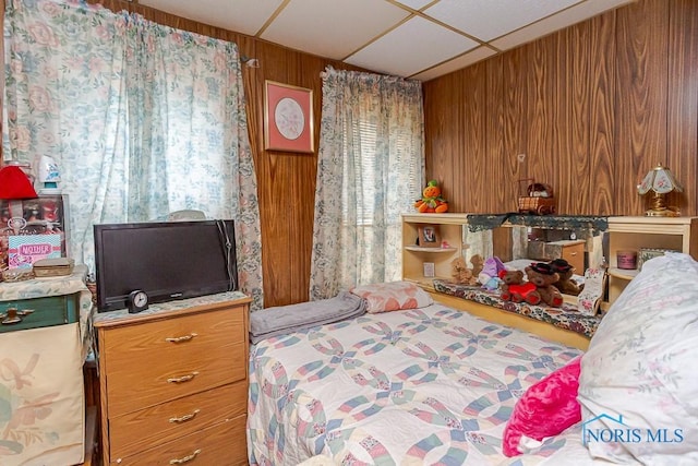 bedroom featuring a drop ceiling and wooden walls