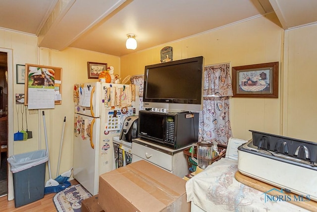 kitchen featuring black microwave, wood finished floors, beam ceiling, freestanding refrigerator, and crown molding