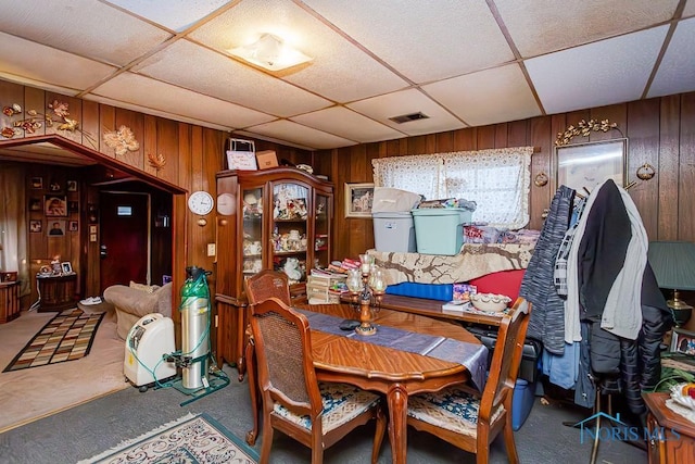 carpeted dining space featuring a paneled ceiling, visible vents, and wooden walls