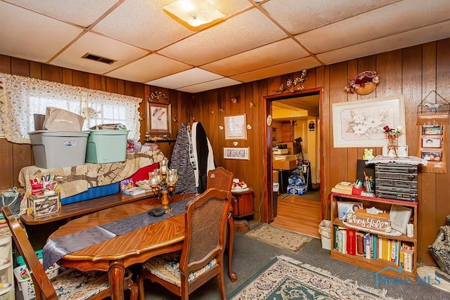 dining room featuring wood walls, a drop ceiling, and visible vents