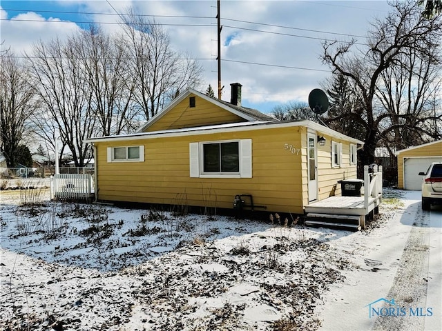 snow covered house with a garage and an outbuilding