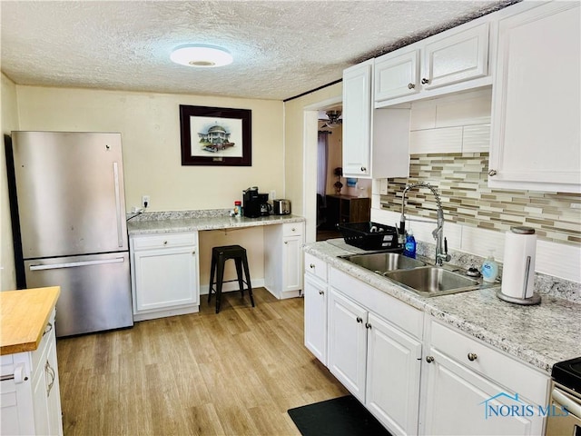 kitchen featuring sink, a textured ceiling, light wood-type flooring, stainless steel refrigerator, and white cabinets