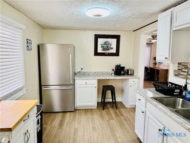 kitchen with stainless steel refrigerator, tasteful backsplash, white cabinets, light hardwood / wood-style floors, and a textured ceiling