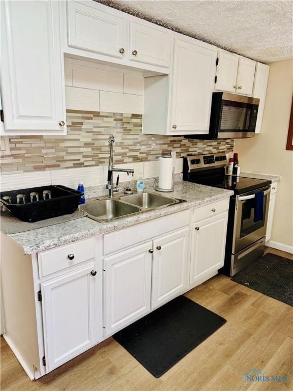 kitchen with sink, white cabinetry, light wood-type flooring, appliances with stainless steel finishes, and backsplash