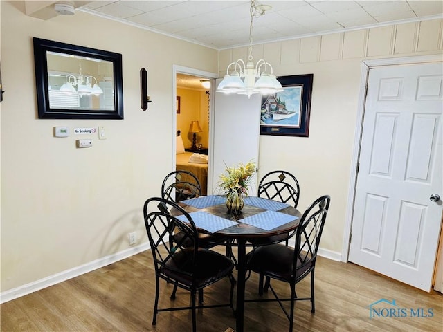 dining area with wood-type flooring, ornamental molding, and a chandelier