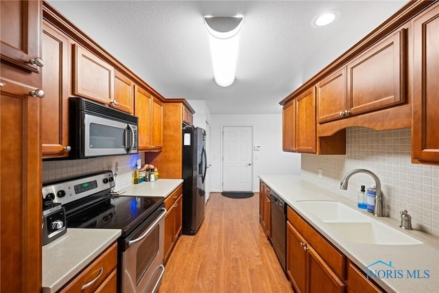 kitchen featuring sink, a textured ceiling, light wood-type flooring, appliances with stainless steel finishes, and decorative backsplash