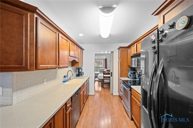 kitchen with sink, a textured ceiling, appliances with stainless steel finishes, light hardwood / wood-style floors, and decorative backsplash