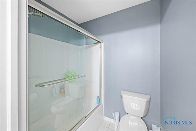 bathroom with tile patterned floors, toilet, and combined bath / shower with glass door