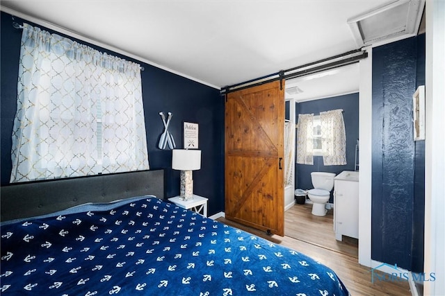 bedroom featuring hardwood / wood-style flooring, ensuite bathroom, and a barn door