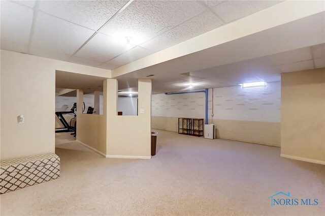 basement with a paneled ceiling, brick wall, and carpet