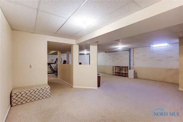 basement with a drop ceiling, brick wall, and carpet