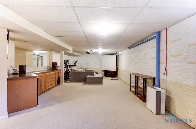 carpeted living room featuring a drop ceiling and brick wall