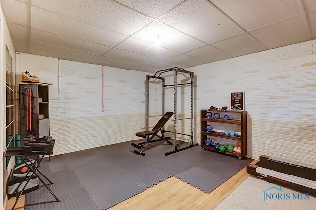 workout area with a drop ceiling, hardwood / wood-style floors, and brick wall