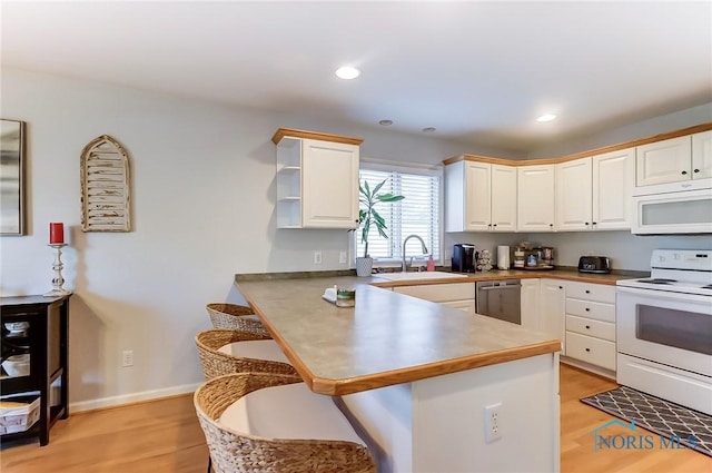 kitchen with sink, white appliances, a kitchen breakfast bar, light hardwood / wood-style floors, and kitchen peninsula