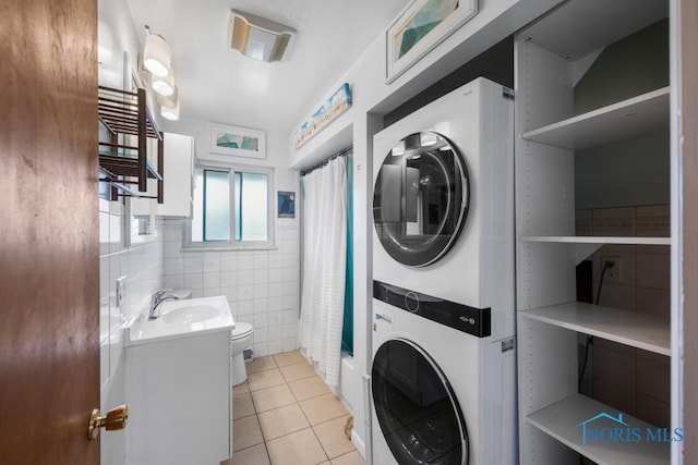 laundry room with stacked washer and dryer, sink, tile walls, and light tile patterned floors