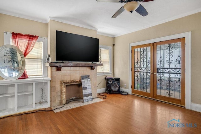 unfurnished living room with ceiling fan, crown molding, a brick fireplace, light wood-type flooring, and french doors