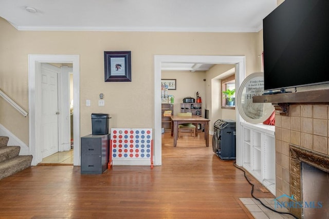 living room featuring a tiled fireplace, hardwood / wood-style floors, and crown molding