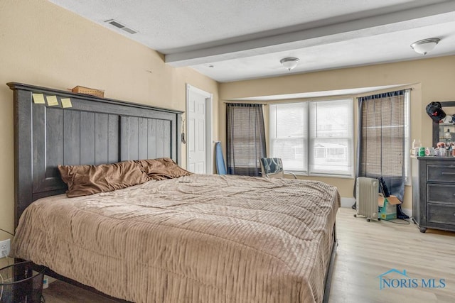 bedroom with beam ceiling, radiator, a textured ceiling, and light hardwood / wood-style floors