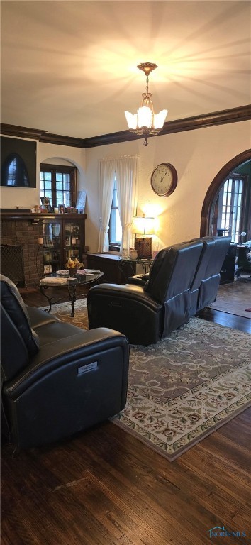 living room with a notable chandelier, crown molding, hardwood / wood-style floors, and a brick fireplace