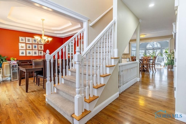 stairs with an inviting chandelier, hardwood / wood-style floors, and a raised ceiling