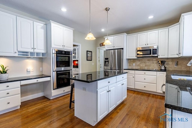 kitchen with sink, appliances with stainless steel finishes, hanging light fixtures, a center island, and white cabinets