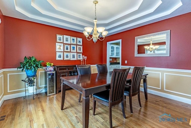 dining area with light hardwood / wood-style flooring, wine cooler, an inviting chandelier, and a tray ceiling