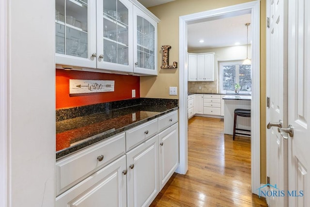 bar featuring backsplash, light hardwood / wood-style flooring, dark stone counters, and white cabinets